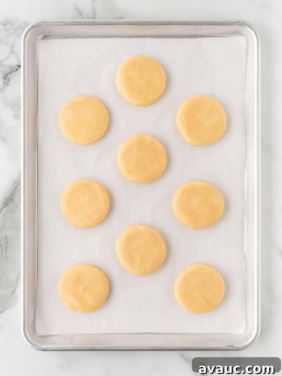 Freshly baked round sugar cookies cooling on a parchment-lined baking sheet