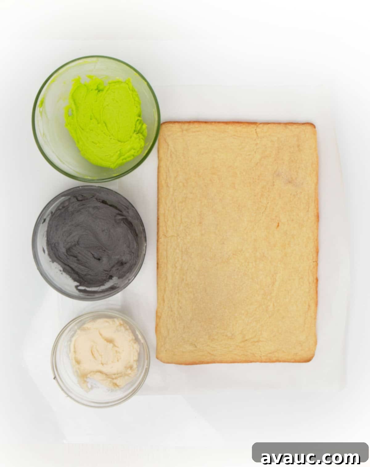 unfrosted sugar cookie bars and bowls of green, black, and white frosting