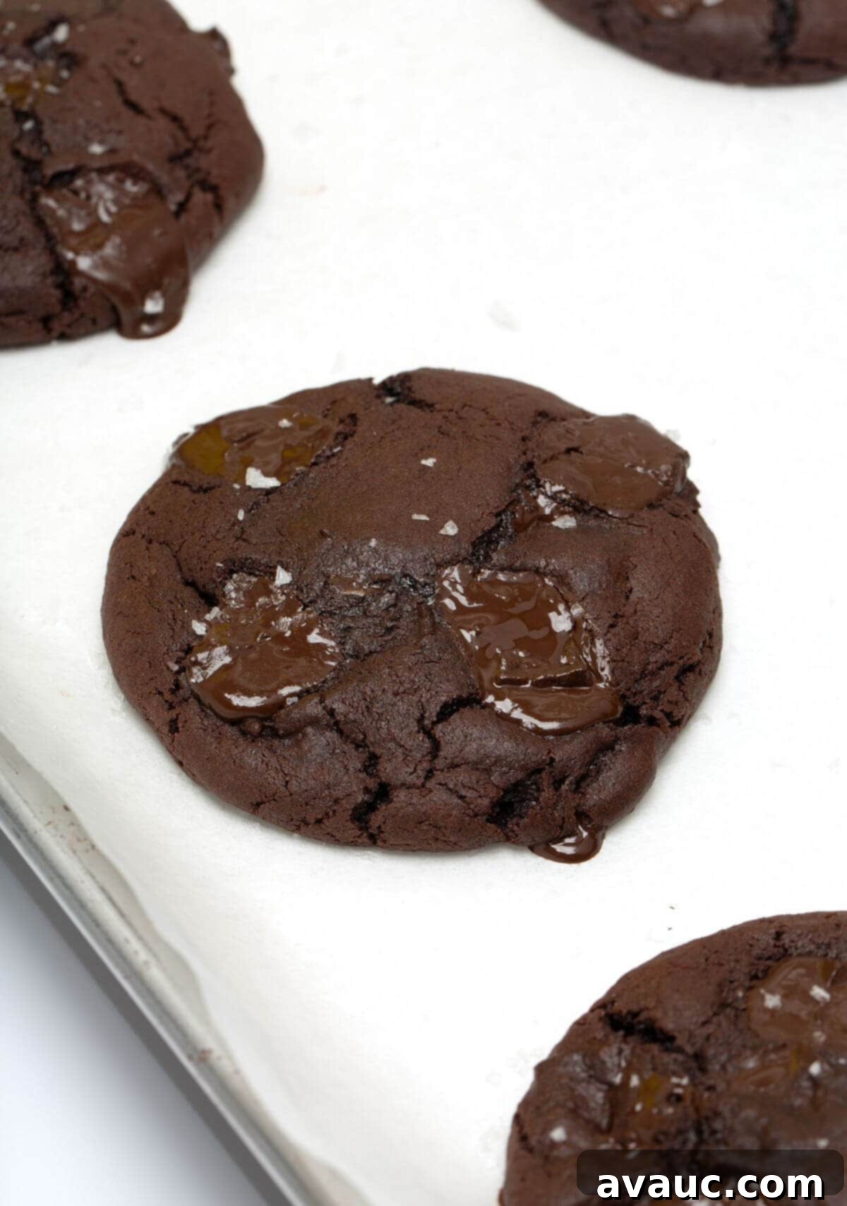 Baked dark chocolate cookie on a parchment-lined baking sheet, glistening with melted chocolate.