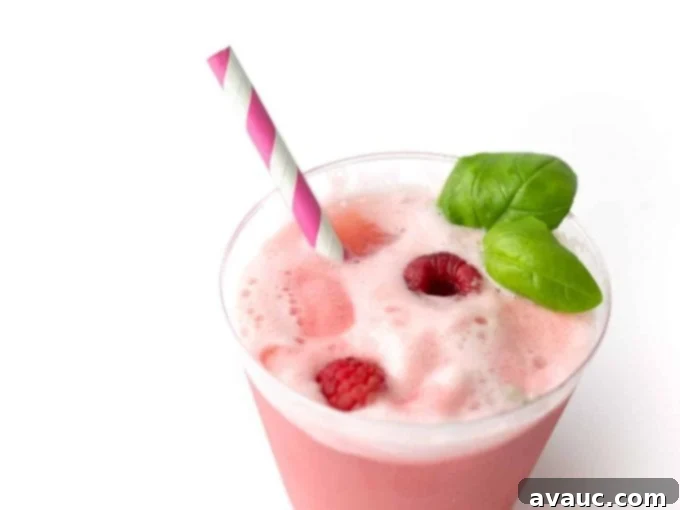 Close-up of a cup of Raspberry Sherbet Punch garnished with fresh raspberries and basil leaves, with a pink straw.