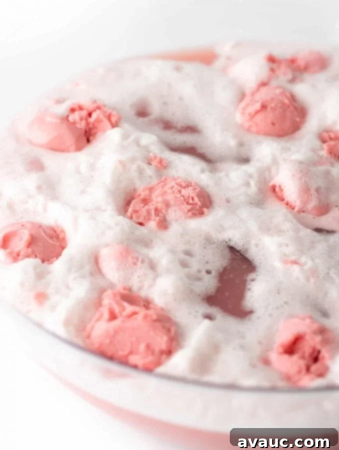 Vibrant Raspberry Sherbet Punch, freshly mixed in a large punch bowl, with a ladle resting inside.