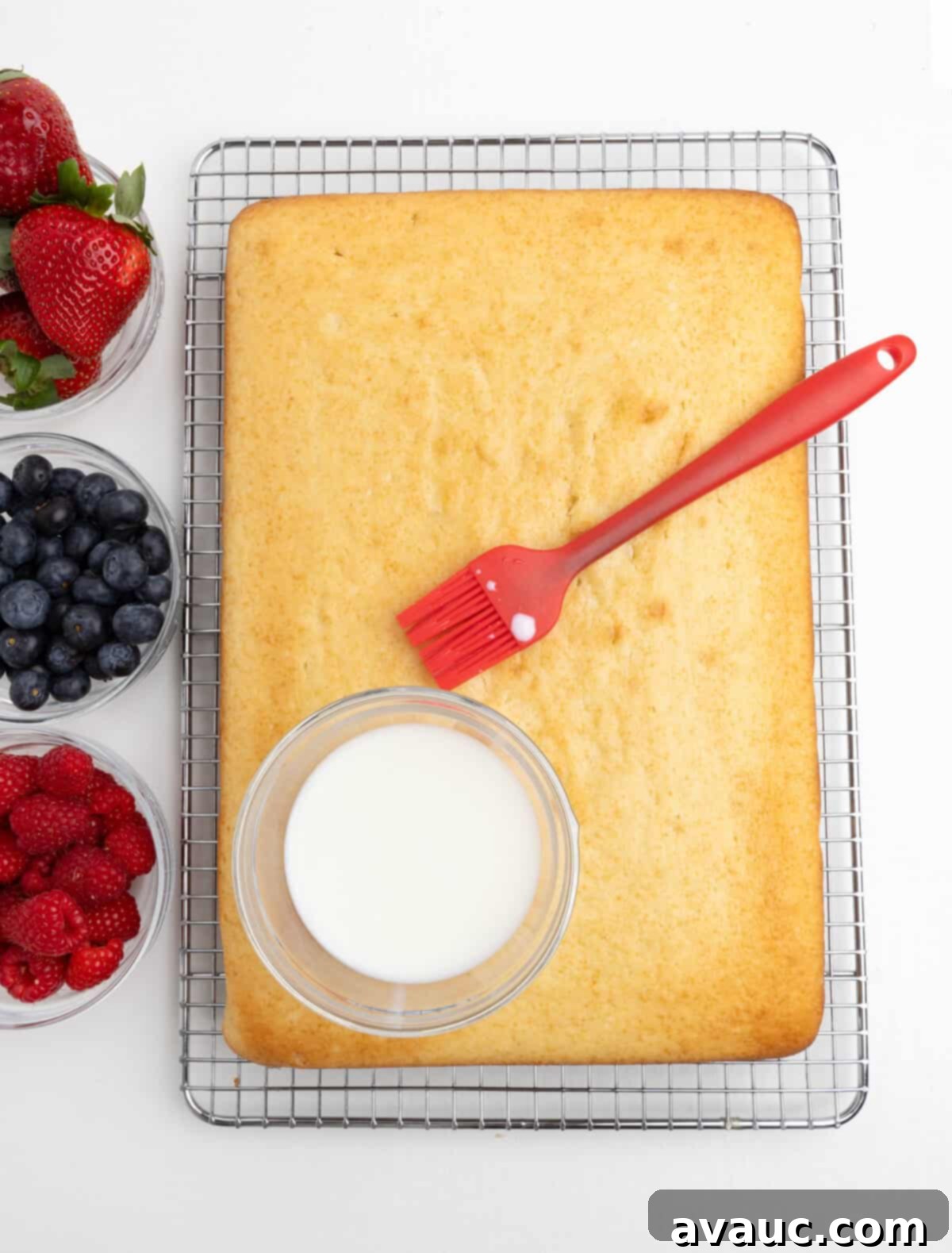 Cake being brushed with a milk soak mixture on a cooling rack