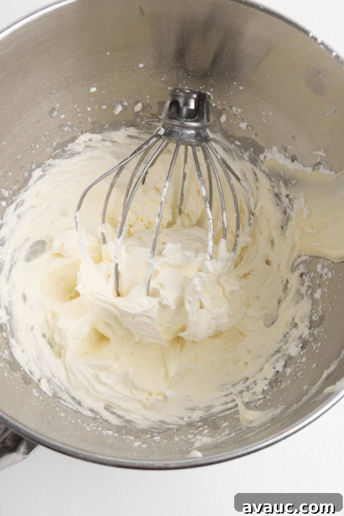 Silky smooth mascarpone frosting being whipped in a large mixing bowl with a whisk attachment
