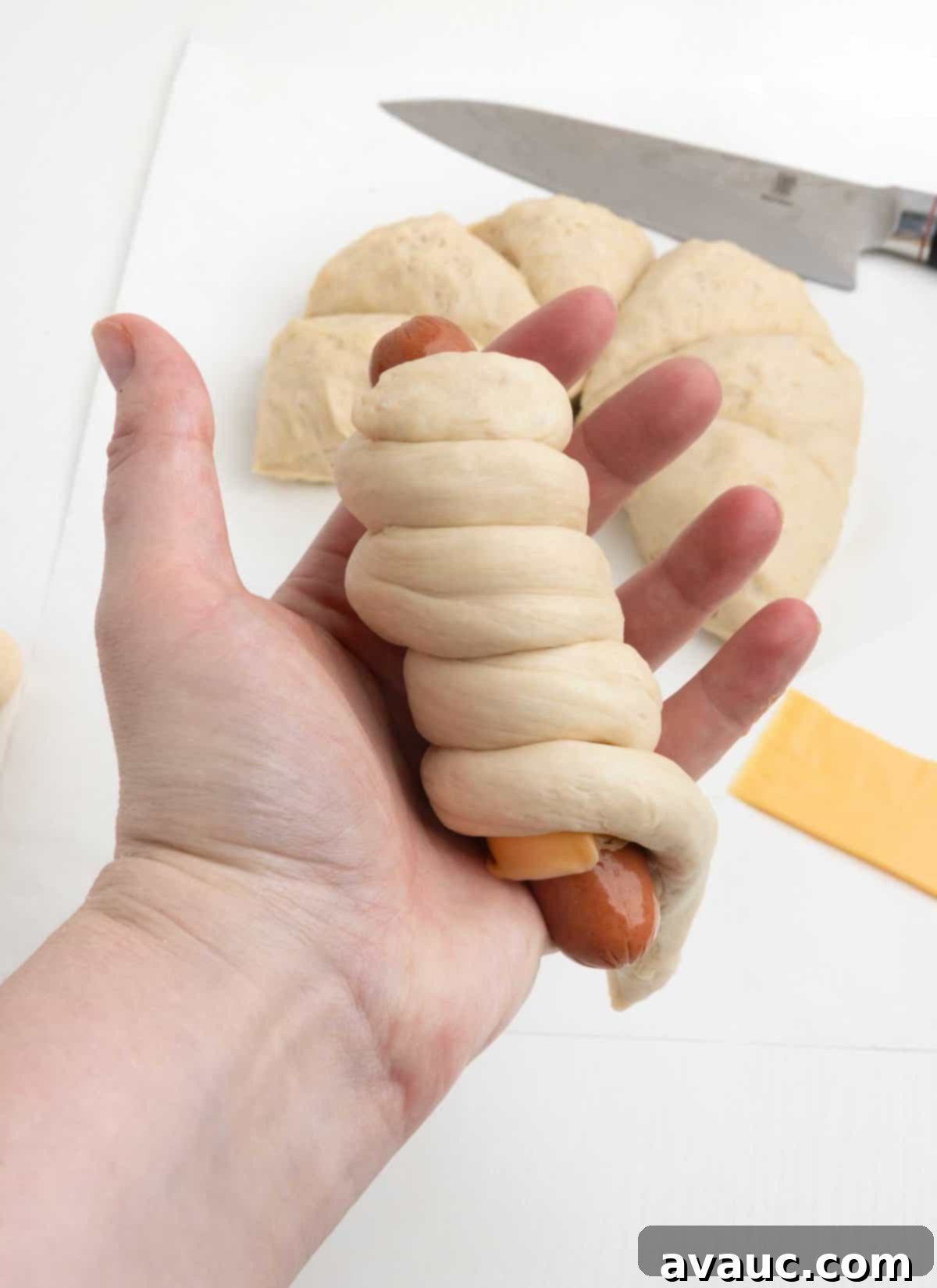 Pretzel Hot Dogs in a Flash 9 Hand holding a hot dog wrapped in pretzel dough, ready for the baking soda bath.