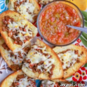 Loaded Cheesy Ground Beef Tortas 9 A plate of two ground beef tortas with melted cheese and fresh cilantro, with a bowl of salsa in the background.