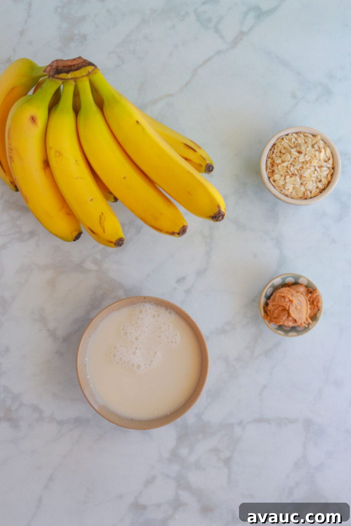 Bananas, a pinch bowl with oats, another with peanut butter and a bowl with almond milk