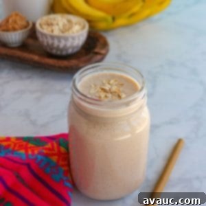 Glass filled with licuado de platano con avena (banana oatmeal smoothie) with a straw beside it and the ingredients behind it