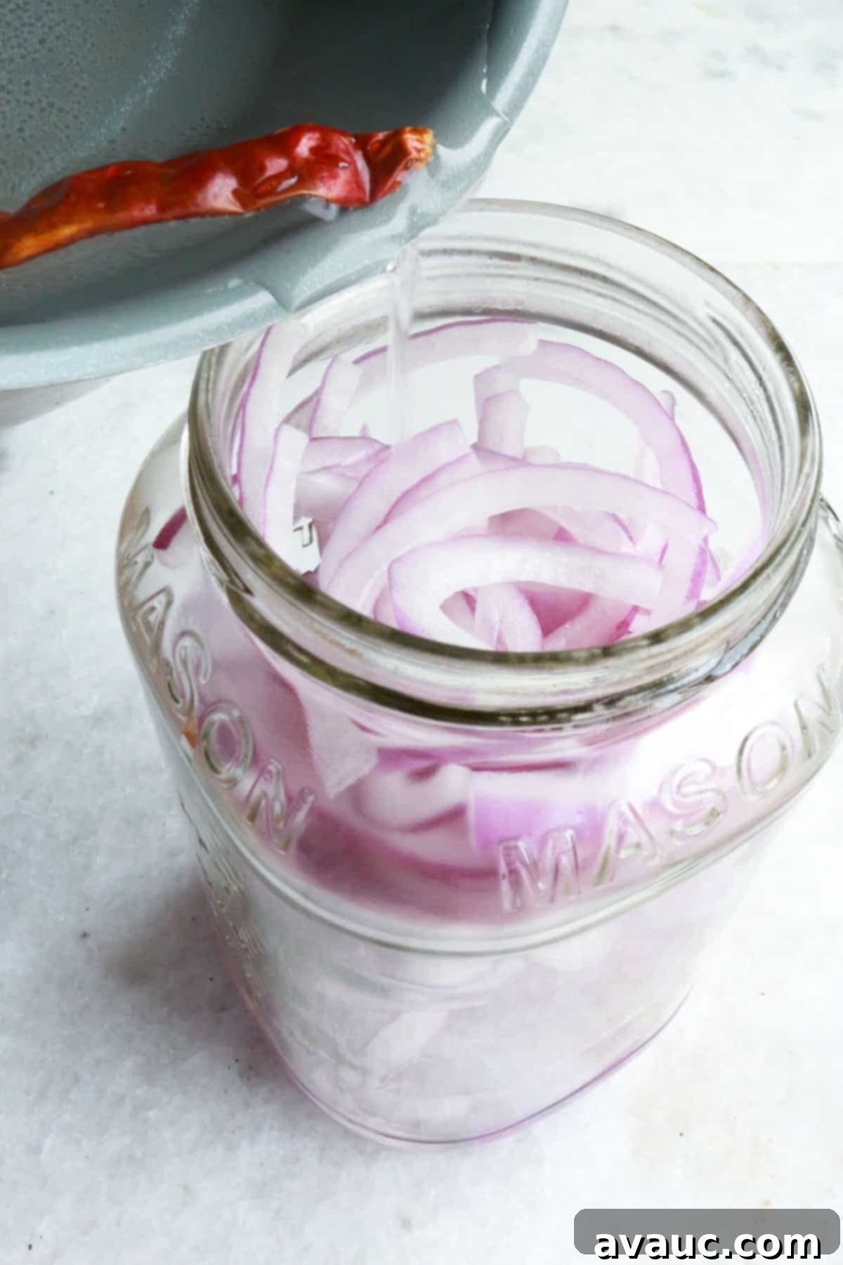 Mexican Pickled Onions 6 Hot pickling brine being poured over thinly sliced red onions packed into a clean mason jar.