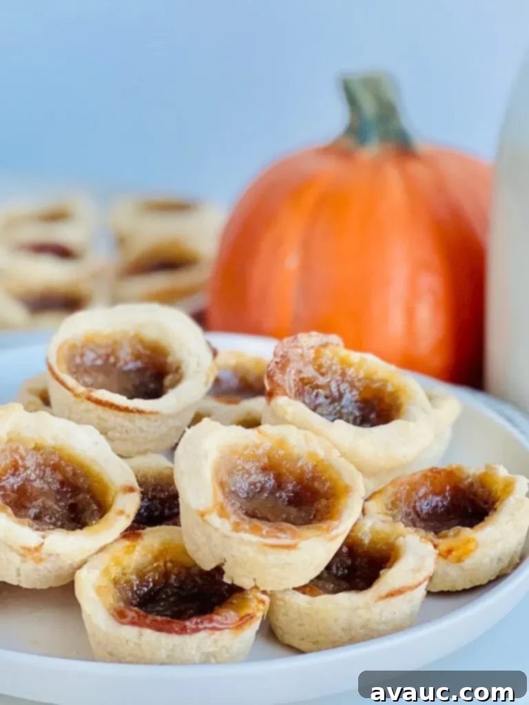 A white plate full of mini little baked tarts filled with a brown sugar gooey mixture with a pumpkin in the background.