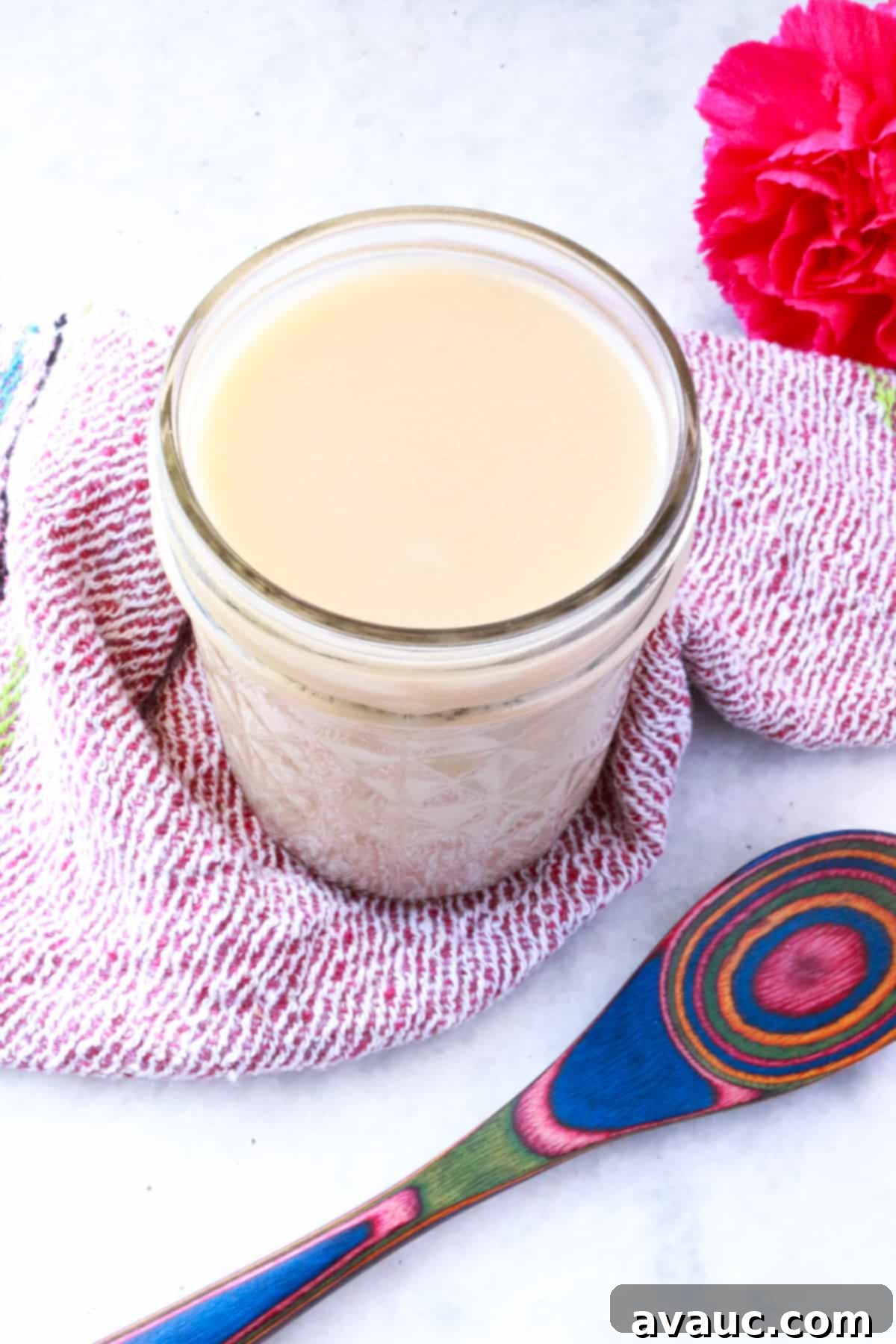 Homemade Coconut Condensed Milk 9 Jar of coconut condensed milk with a pink flower behind it and a colorful wooden spoon in front of it.
