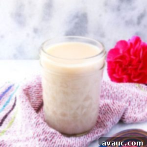 Homemade Coconut Condensed Milk 10 Jar of coconut condensed milk with a pink flower behind it and a colorful wooden spoon in front of it.