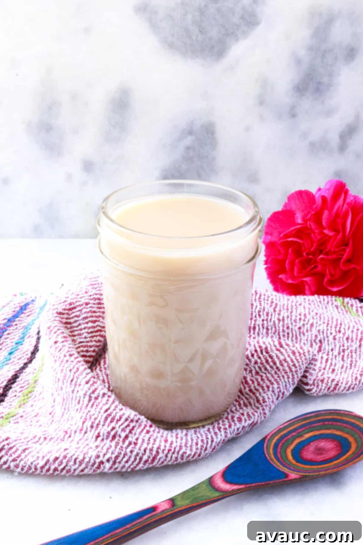 Homemade Coconut Condensed Milk 2 Jar of coconut condensed milk with a pink flower behind it and a colorful wooden spoon in front of it.