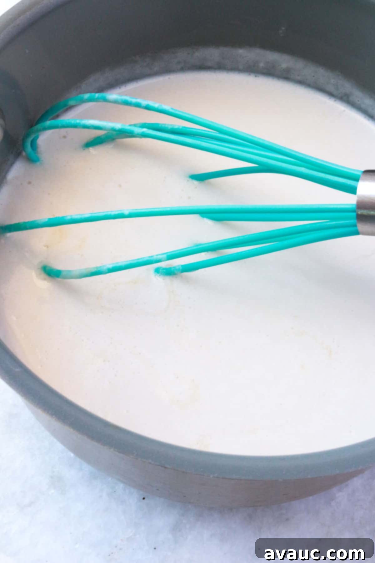 Homemade Coconut Condensed Milk 6 Coconut milk simmering in a small pot with a whisk