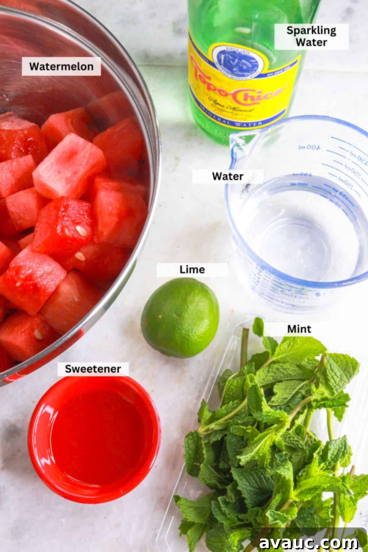 Ingredients for sparkling watermelon agua fresca: Bowl with pieces of watermelon, a bottle of Topo Chico, measuring cup with water, a lime, mint leaves and a small bowl with agave syrup