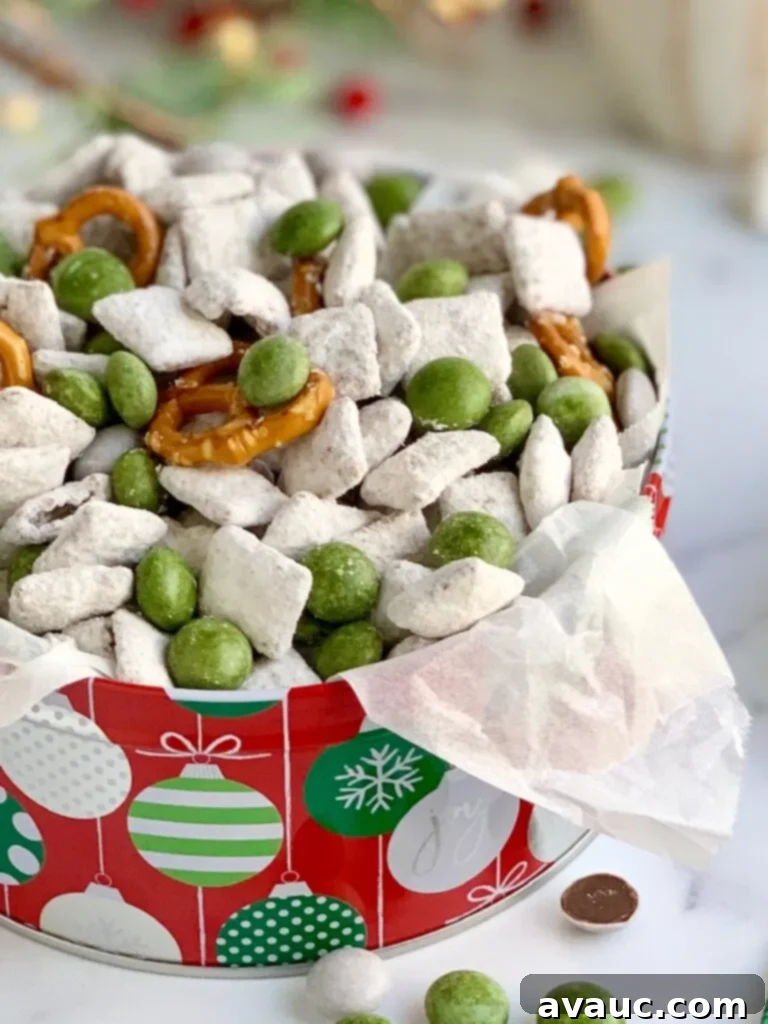 A festive tin filled with a colorful mix of puppy chow, savory pretzels, and vibrant white and green peppermint candies.
