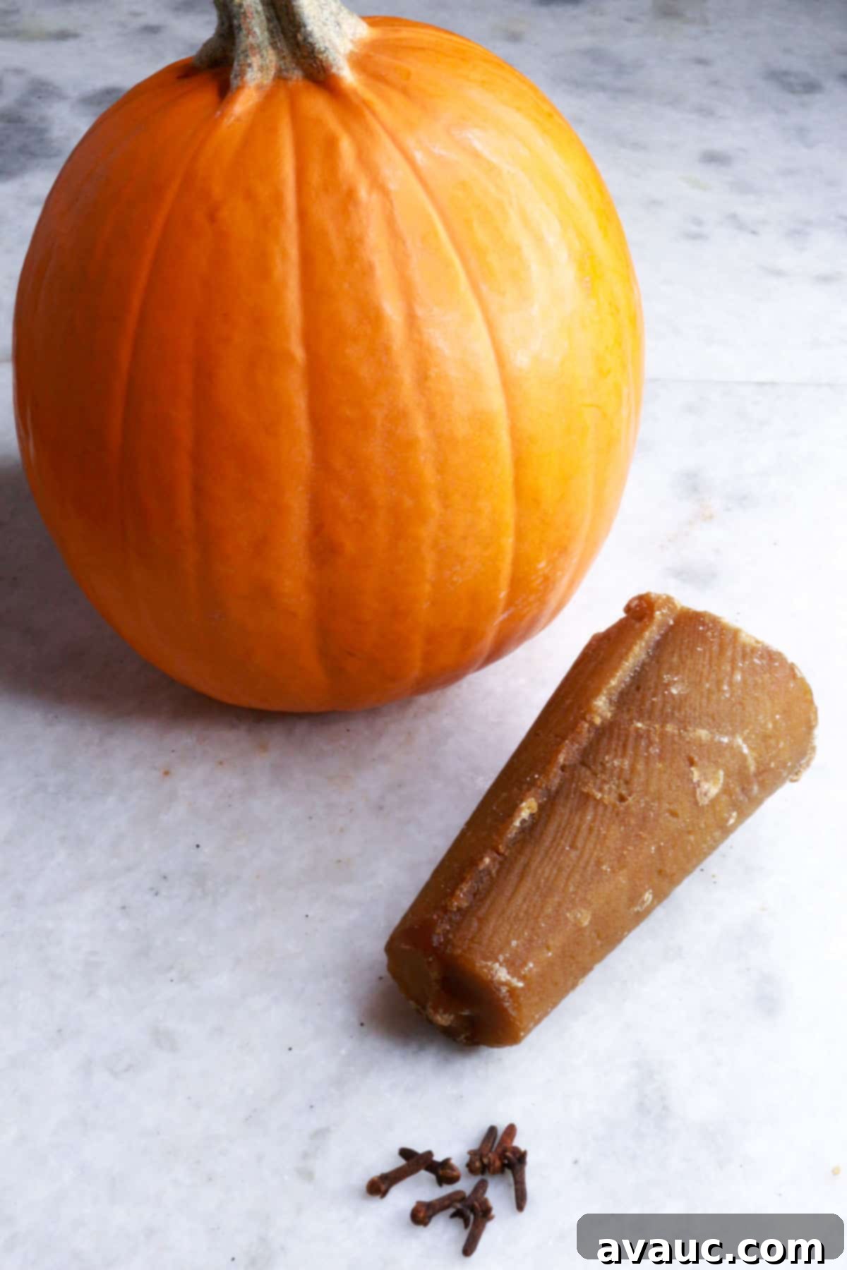 Pumpkin Empanada Filling 3 A whole pie pumpkin, a cone of piloncillo sugar, and whole cloves arranged on a white background, highlighting key ingredients for pumpkin puree.