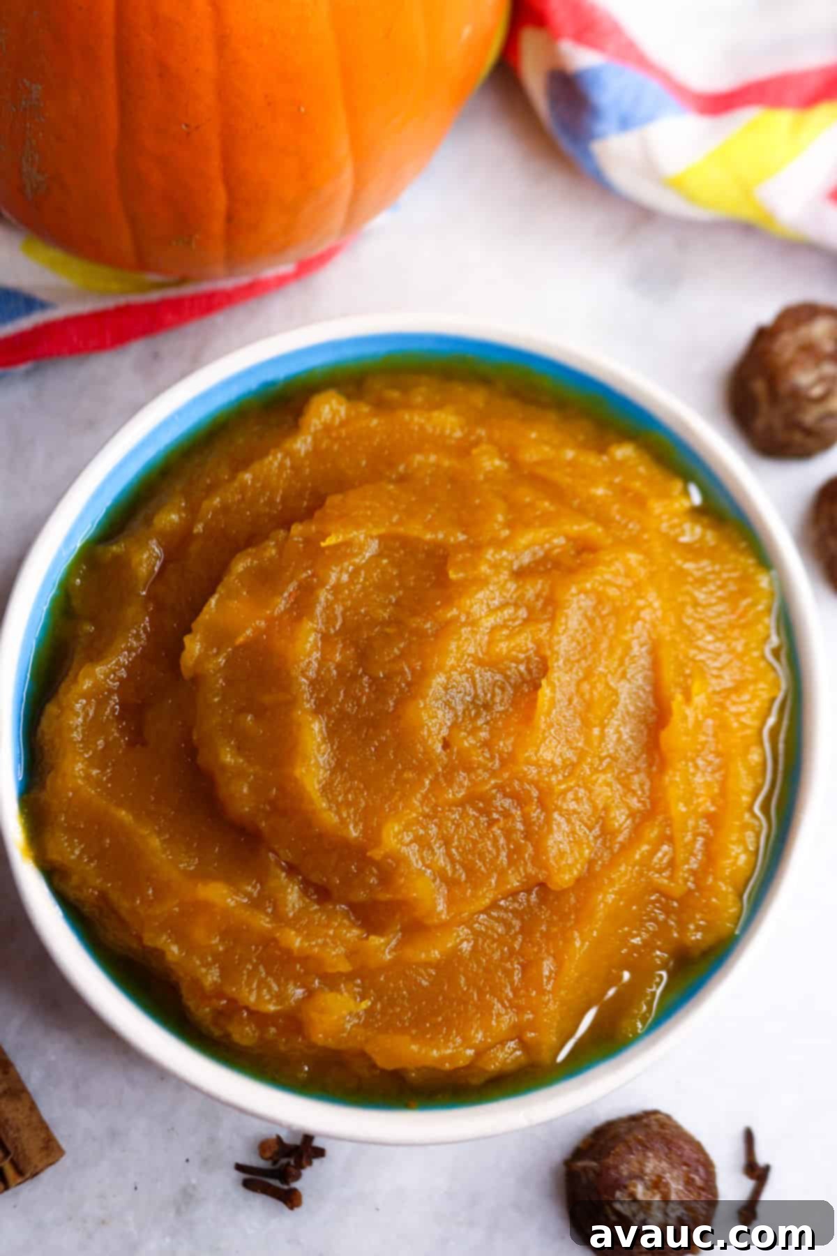 Pumpkin Empanada Filling 10 A beautifully arranged bowl of Puré de Calabaza, surrounded by small piloncillo cones, a fresh pumpkin, cinnamon sticks, and whole cloves, creating an inviting fall scene.