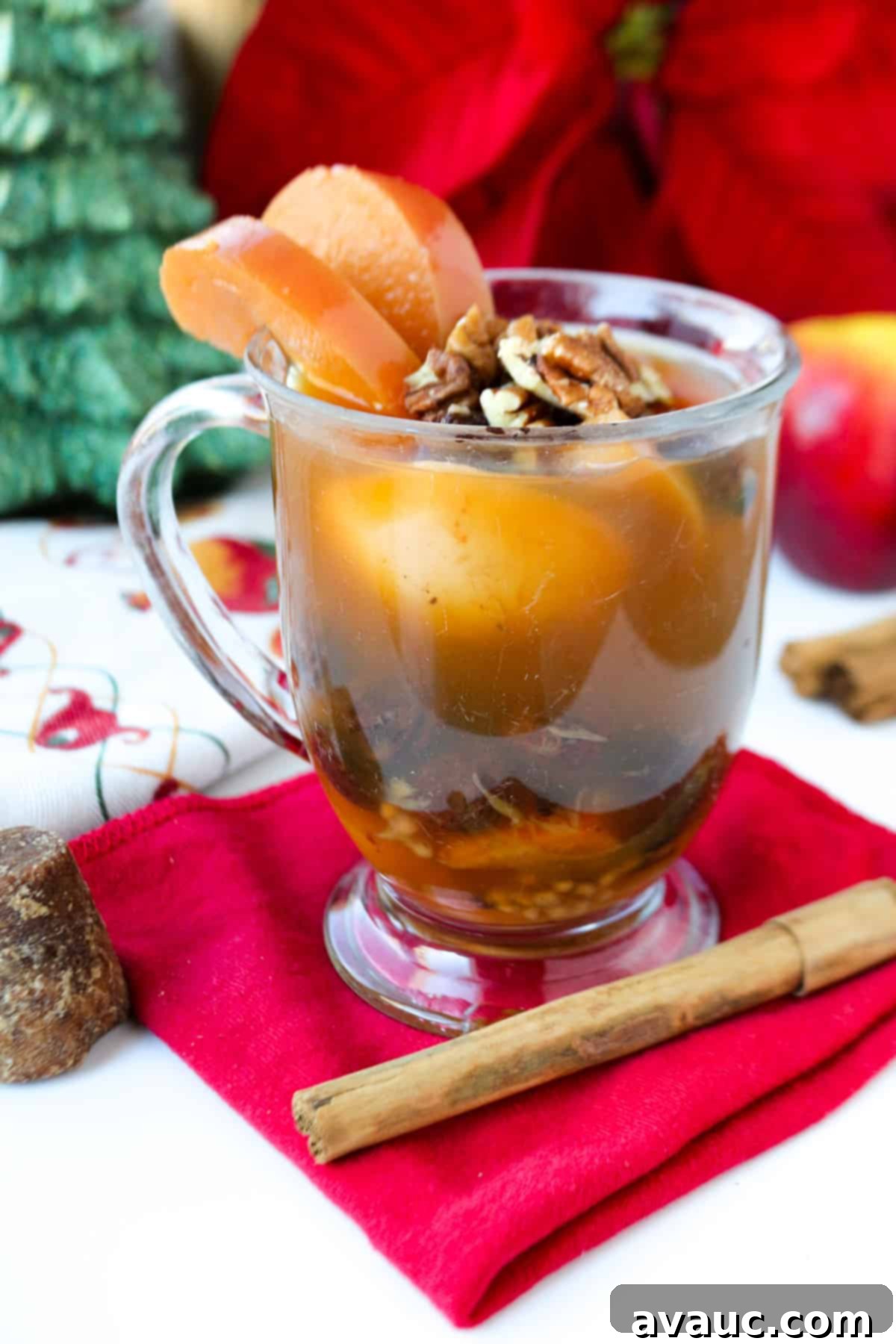 Clear glass with ponche Navideño and garnished with pecans and fruit in front of Christmas decorations