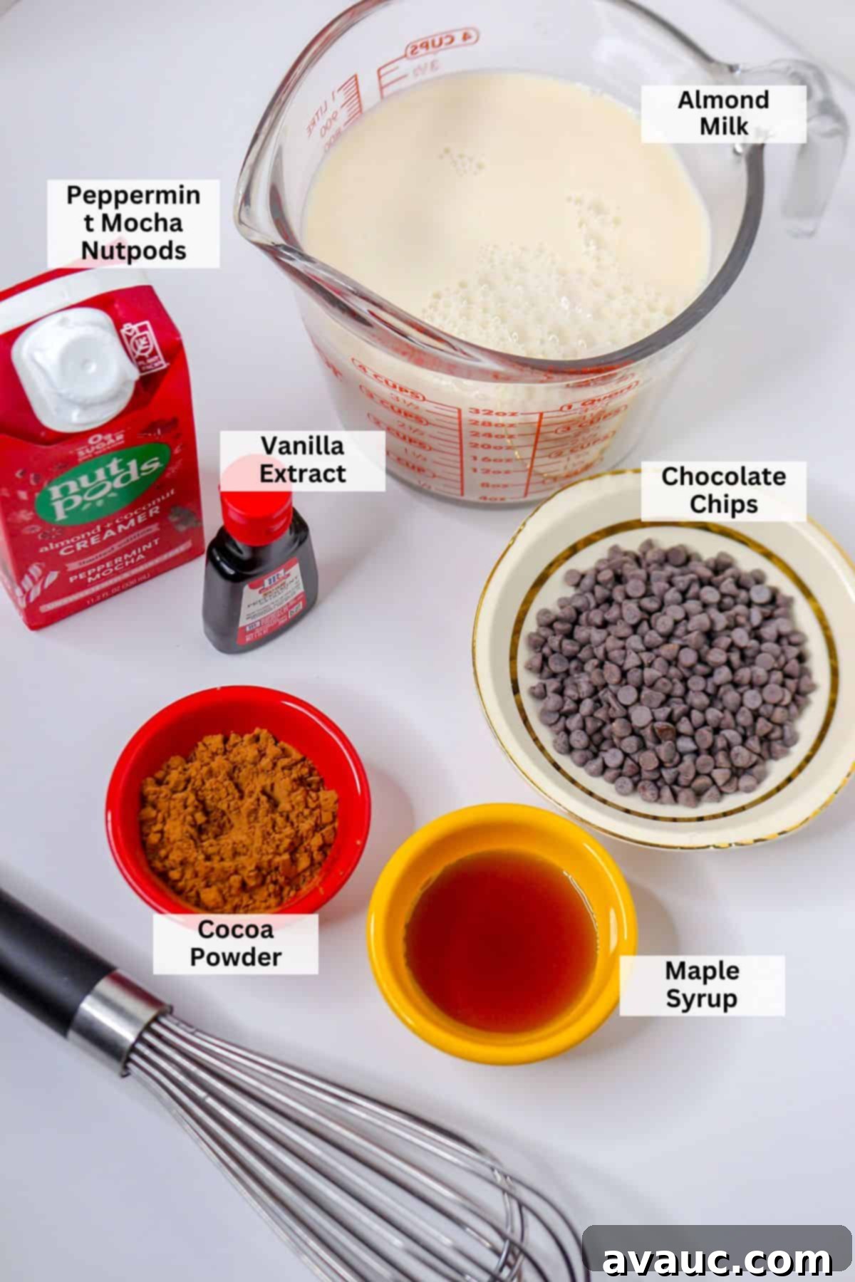Homemade Plant-Based Peppermint Hot Chocolate 3 Ingredients for homemade peppermint hot chocolate: almond milk, peppermint mocha creamer, vanilla extract, cocoa powder, chocolate chips, maple syrup laid out on a wooden surface.