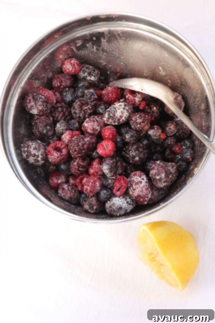 Effortless Gluten-Free Dump Cake 4 Berries in a mixing bowl with. spoon and half of a lemon beside it