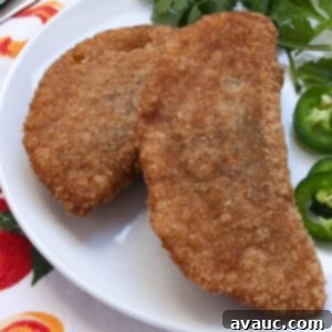 Savory Gluten-Free Sardine Empanadas 11 Two gluten-free empanadas de sardina on a plate with cilantro and jalapeño slices beside them.