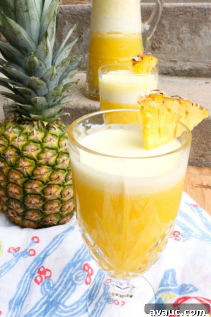 Fresh Pineapple Cooler 2 Close-up of a glass pitcher filled with golden pineapple agua fresca and fresh pineapple slices, garnished with mint.