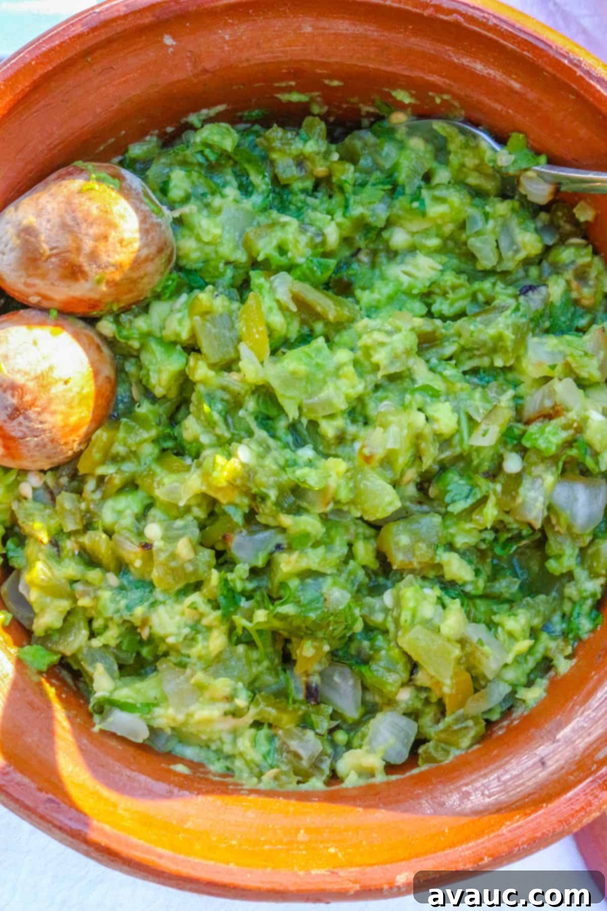 Smoky Roasted Green Chile Guacamole 2 Roasted Green Chile Guacamole in a brown Mexican bowl, garnished with fresh cilantro and a lime wedge