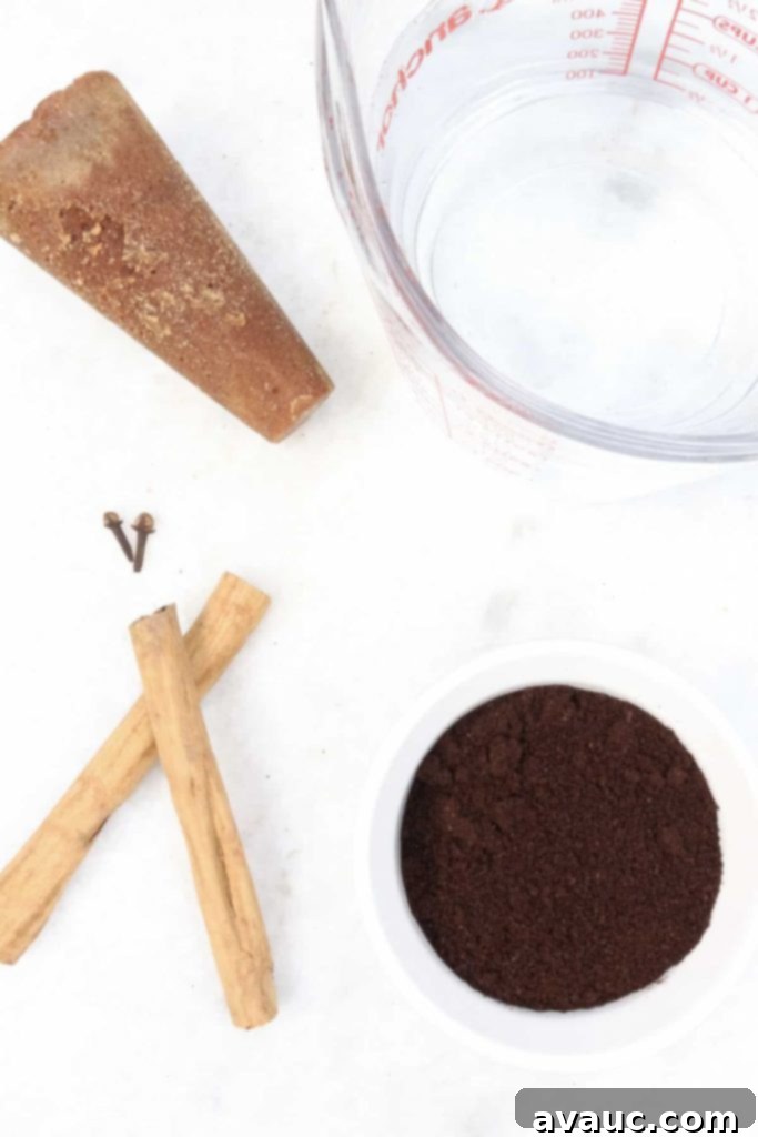 Authentic Café de Olla Recipe 3 Piloncillo cone, a measuring cup with water, cloves, cinnamon sticks and ground coffee on a white background.