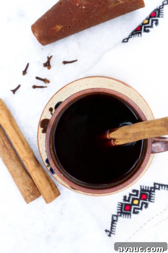 Authentic Café de Olla Recipe 7 Cafe de Olla from above in a pottery mug with a cinnamon stick and surrounded by piloncillo, cinnamon sticks and cloves.