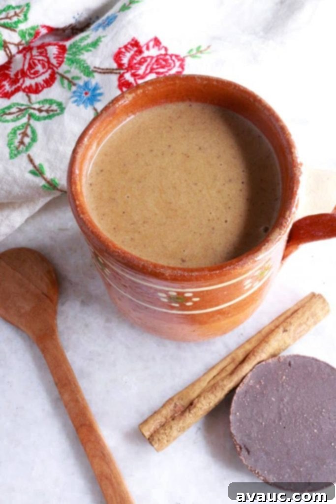 Authentic Mexican Champurrado 2 Mug of Mexican Champurrado with wooden spoon, cinnamon stick and Mexican chocolate beside it