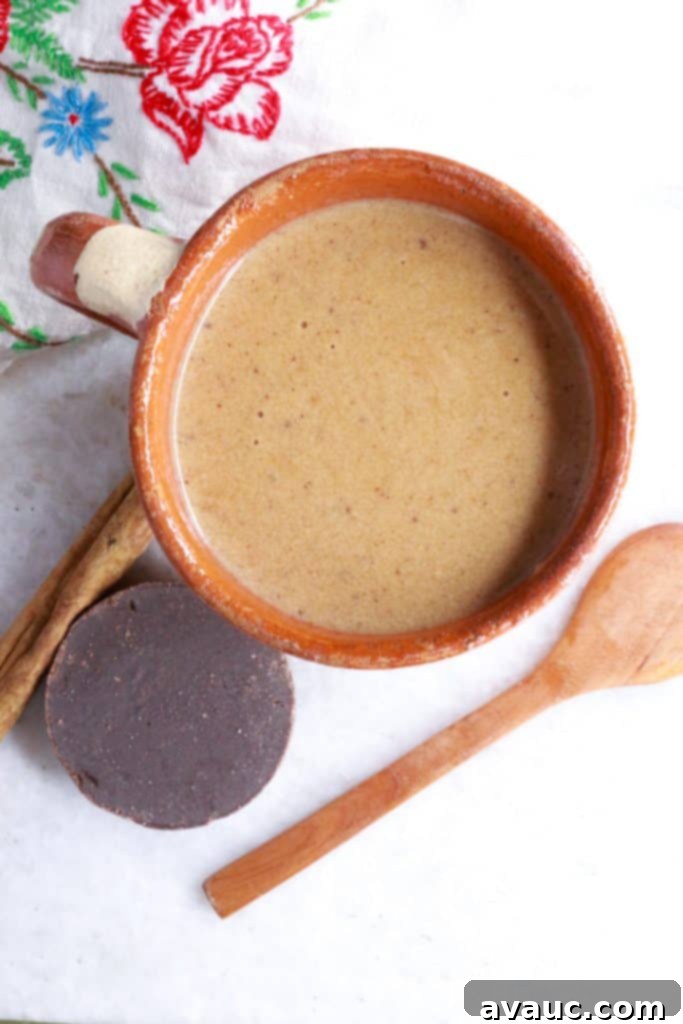 Authentic Mexican Champurrado 9 Mug of Mexican Champurrado with wooden spoon, cinnamon stick and Mexican chocolate beside it