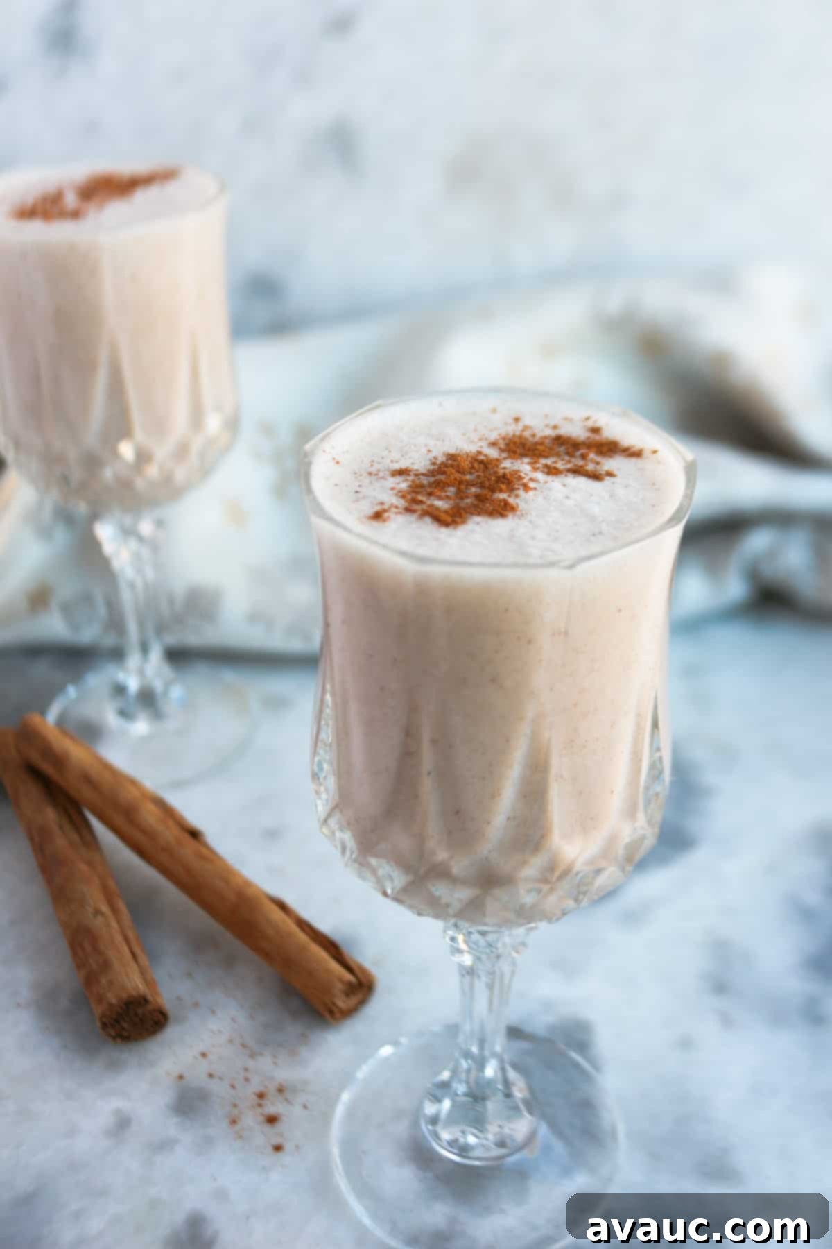 Creamy Vegan Coquito 2 Two clear and small wine glasses filled with coquito with cinnamons sticks beside them.