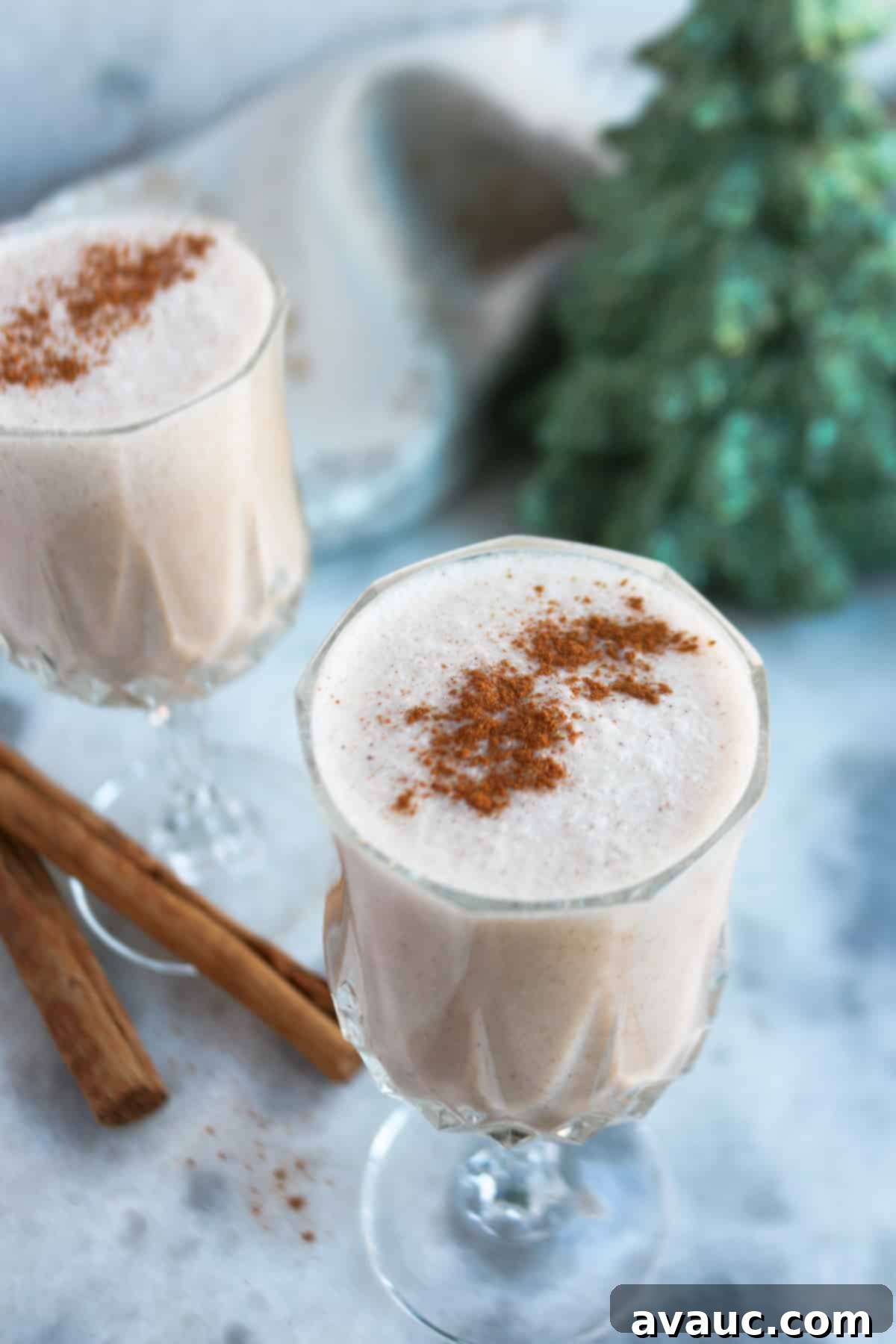 Creamy Vegan Coquito 7 Two clear glasses with Puerto Rican coquito and sprinkled with cinnamon powder, with two cinnamons sticks beside them.