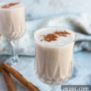 Creamy Vegan Coquito 8 Two clear and small wine glasses filled with coquito with cinnamons sticks beside them.