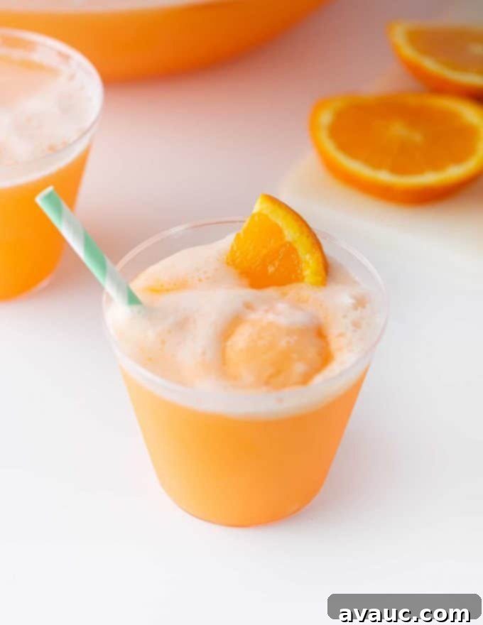 Creamy Orange Fizz 3 A close-up shot of a glass of Orange Sherbet Punch, showing its frothy texture and vibrant orange color, garnished with an orange slice.