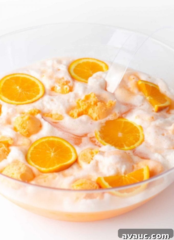 Creamy Orange Fizz 7 Punch bowl filled with Orange Sherbet Punch, garnished with floating orange slices and sherbet scoops, ready for serving.
