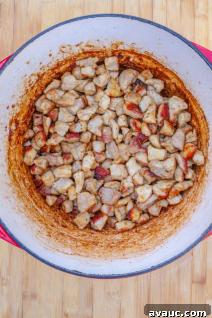 A Dutch oven containing perfectly browned and caramelized diced pork, forming the flavorful base for the green chile stew.