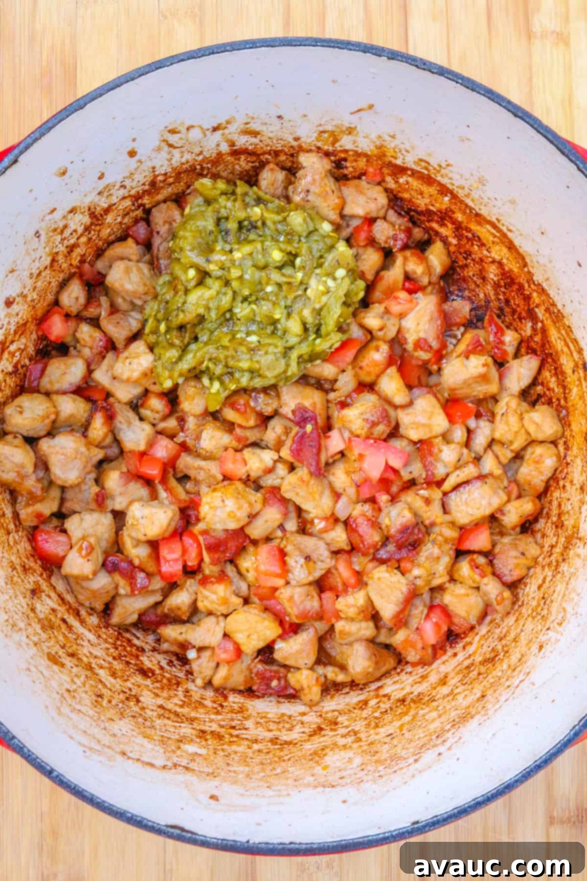 A Dutch oven filled with browned diced pork, sautéed aromatics, and vibrant diced green chiles, beginning to meld their flavors.