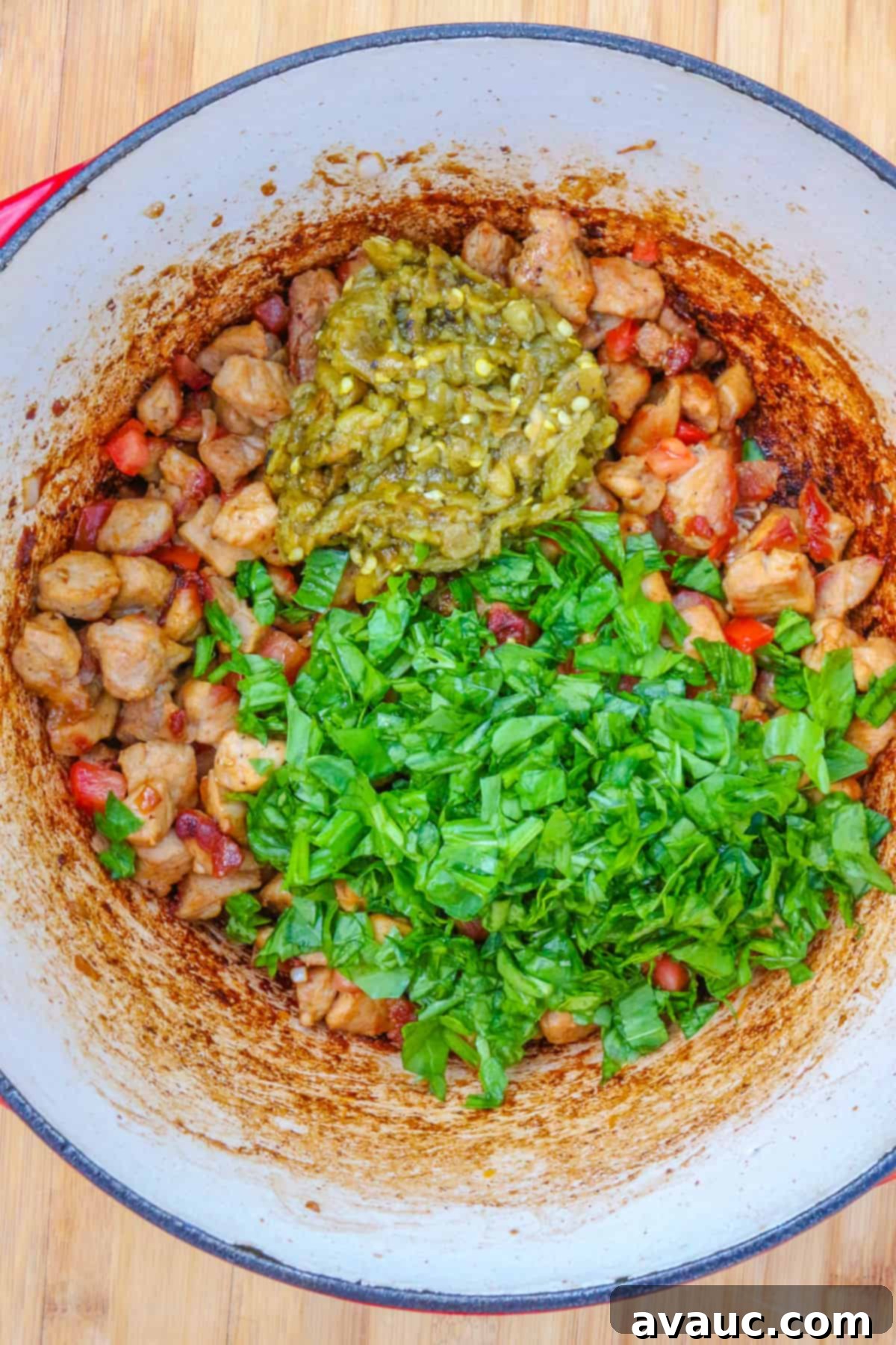 A Dutch oven with the pork green chile base, now incorporating a generous amount of fresh spinach, which is just beginning to wilt into the flavorful stew.