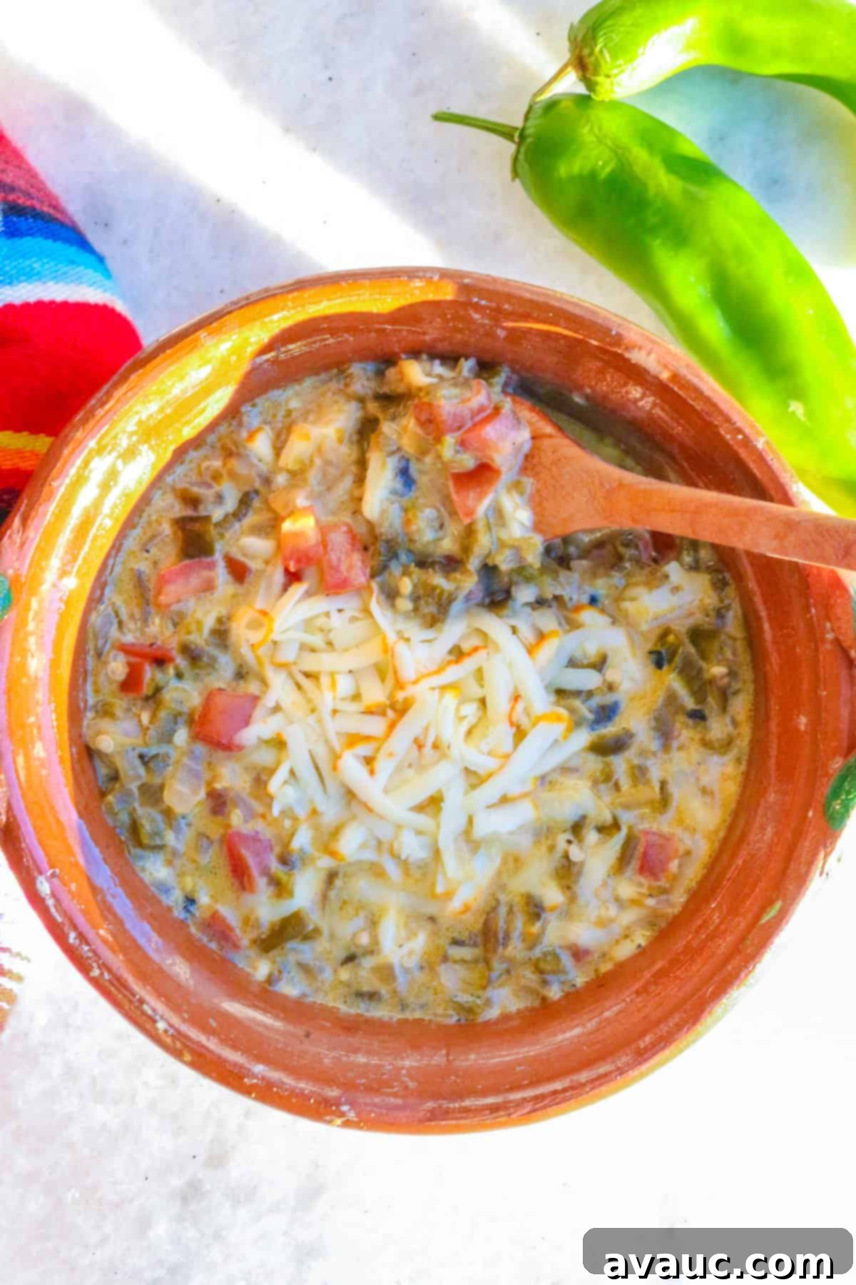 Zesty Green Chile and Melted Cheese 10 Top view of a Mexican brown bowl of Chile Verde con Queso (green chile with cheese) with a wooden spoon