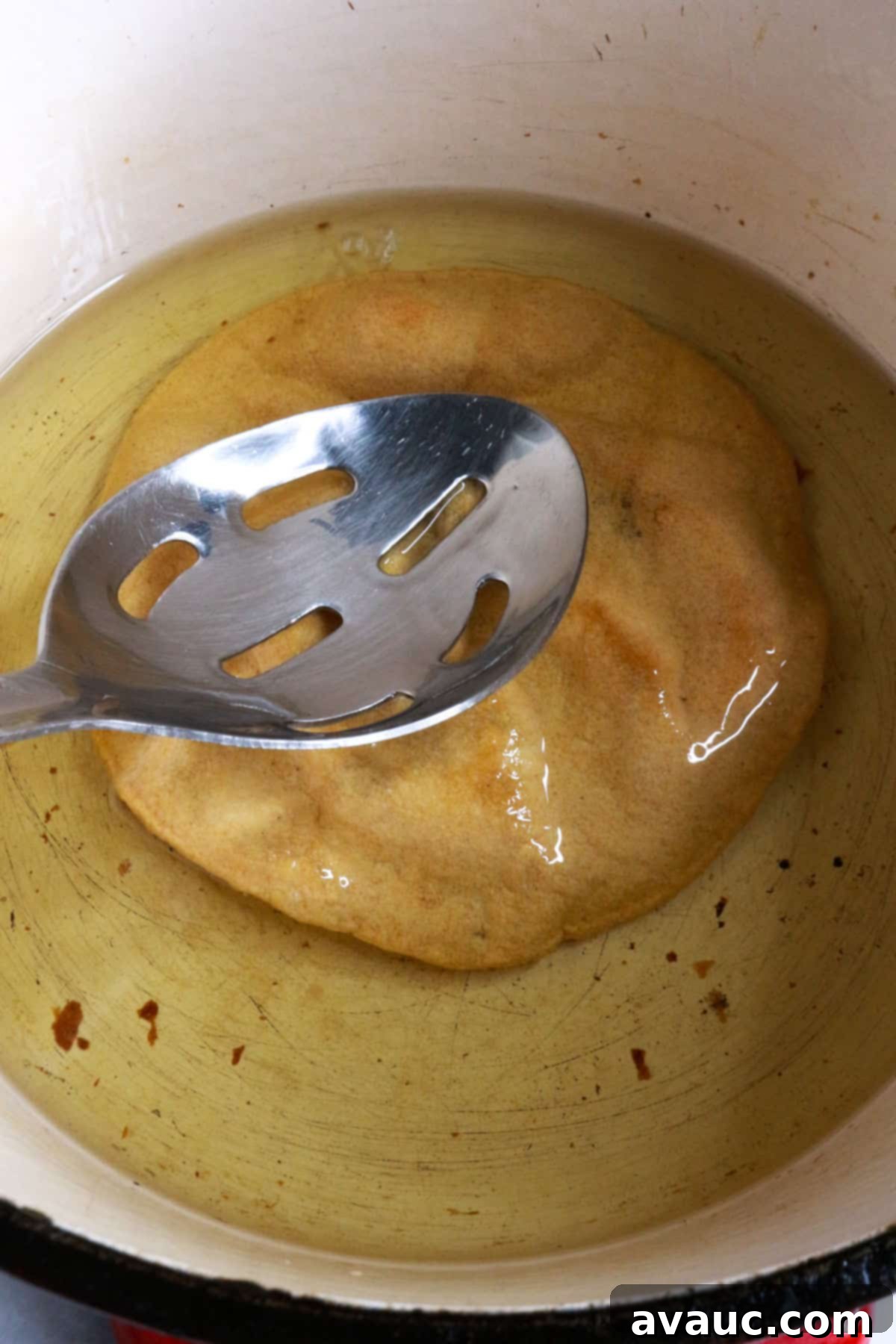 Homemade Tostada Shells Made Easy 5 A corn tortilla being gently pressed into hot oil with a slotted spoon to ensure even frying