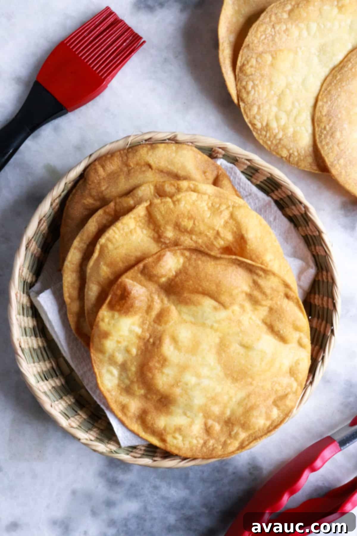 Homemade Tostada Shells Made Easy 10 Freshly made tostada shells artfully arranged on a white surface, accompanied by a pastry brush and tongs