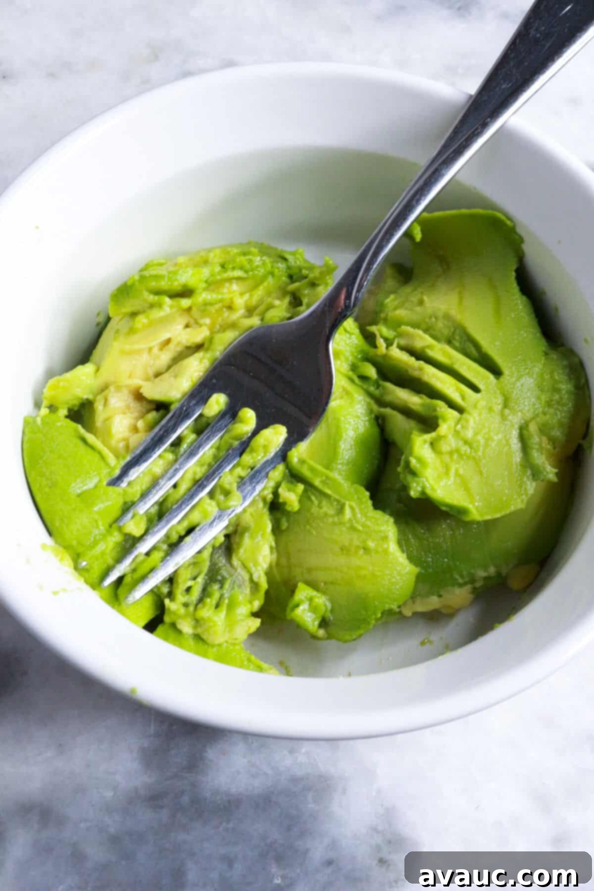 Delicious Avocado Tostadas 5 A close-up shot of a fork expertly mashing a ripe avocado in a bowl, creating a creamy base for tostadas.