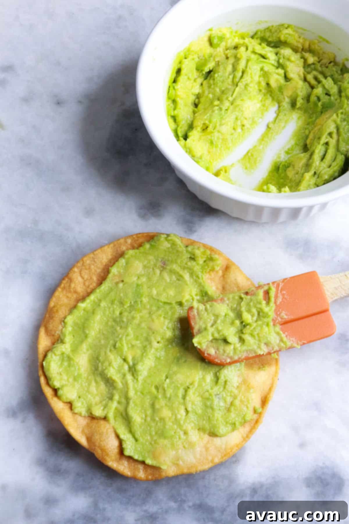 Delicious Avocado Tostadas 6 A hand carefully spreading creamy mashed avocado onto a crispy tostada shell, preparing the base for additional toppings.