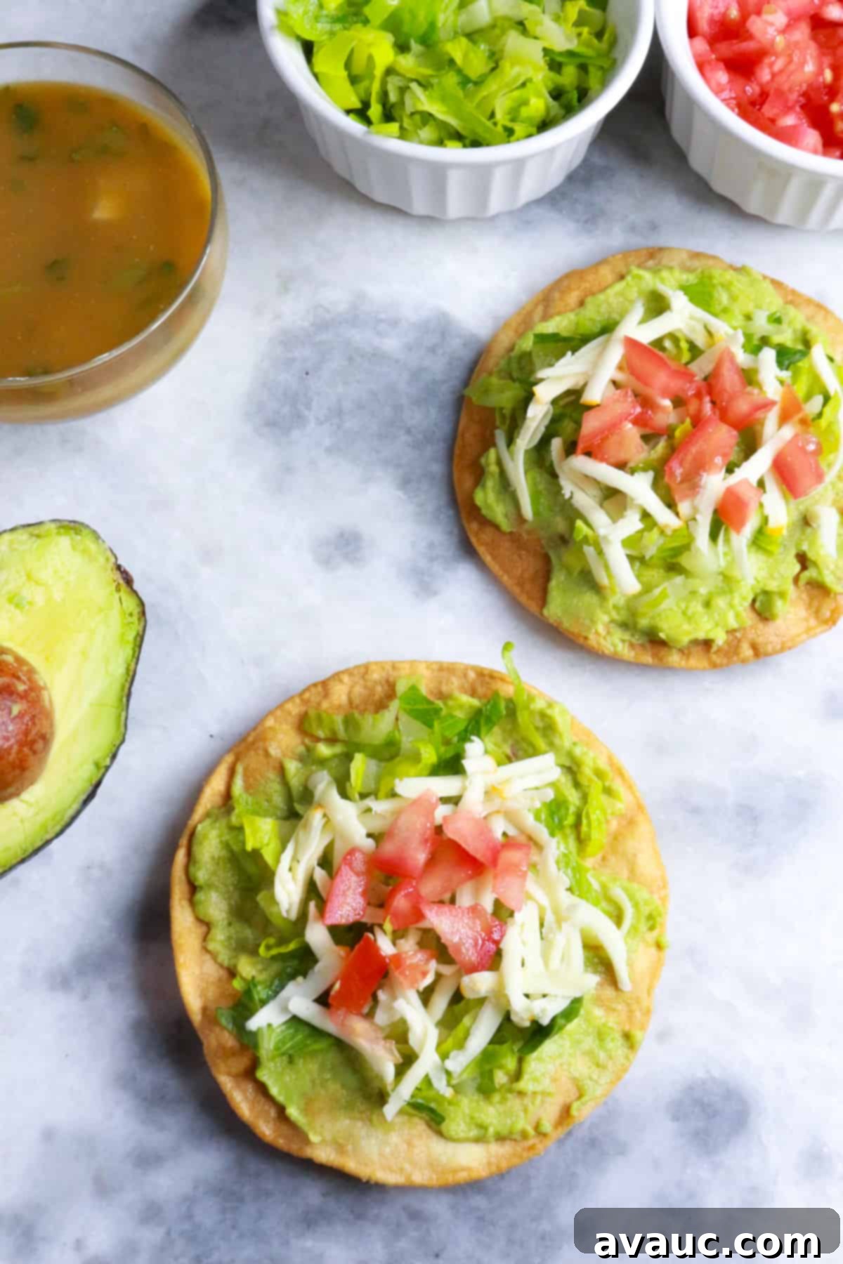 Delicious Avocado Tostadas 7 A vibrant platter of avocado tostadas, garnished with fresh tomato and lettuce, served alongside a container of zesty salsa and a perfectly halved avocado.