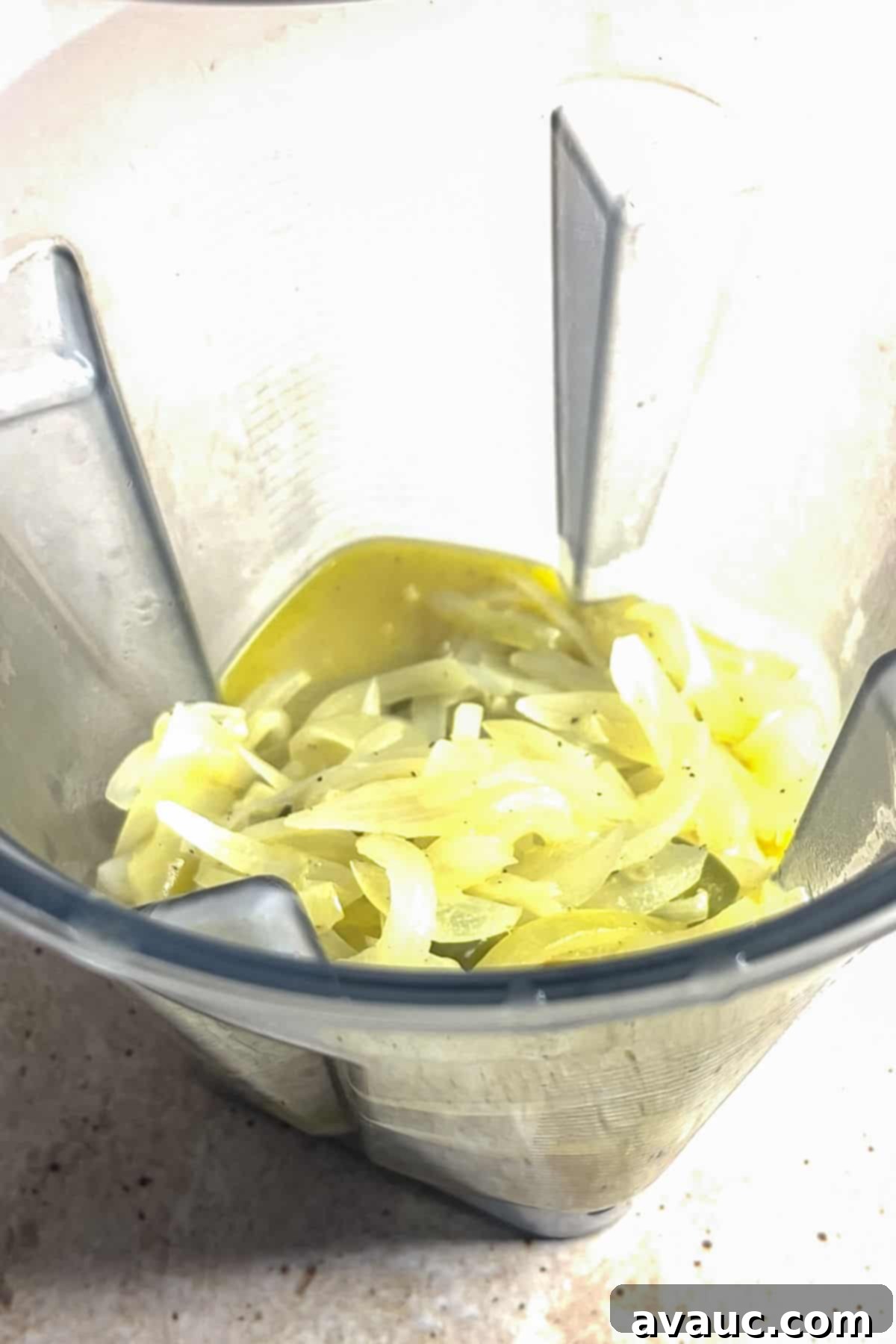 Adding cooked onion and jalapeño mixture to a blender for creamy onion soup.