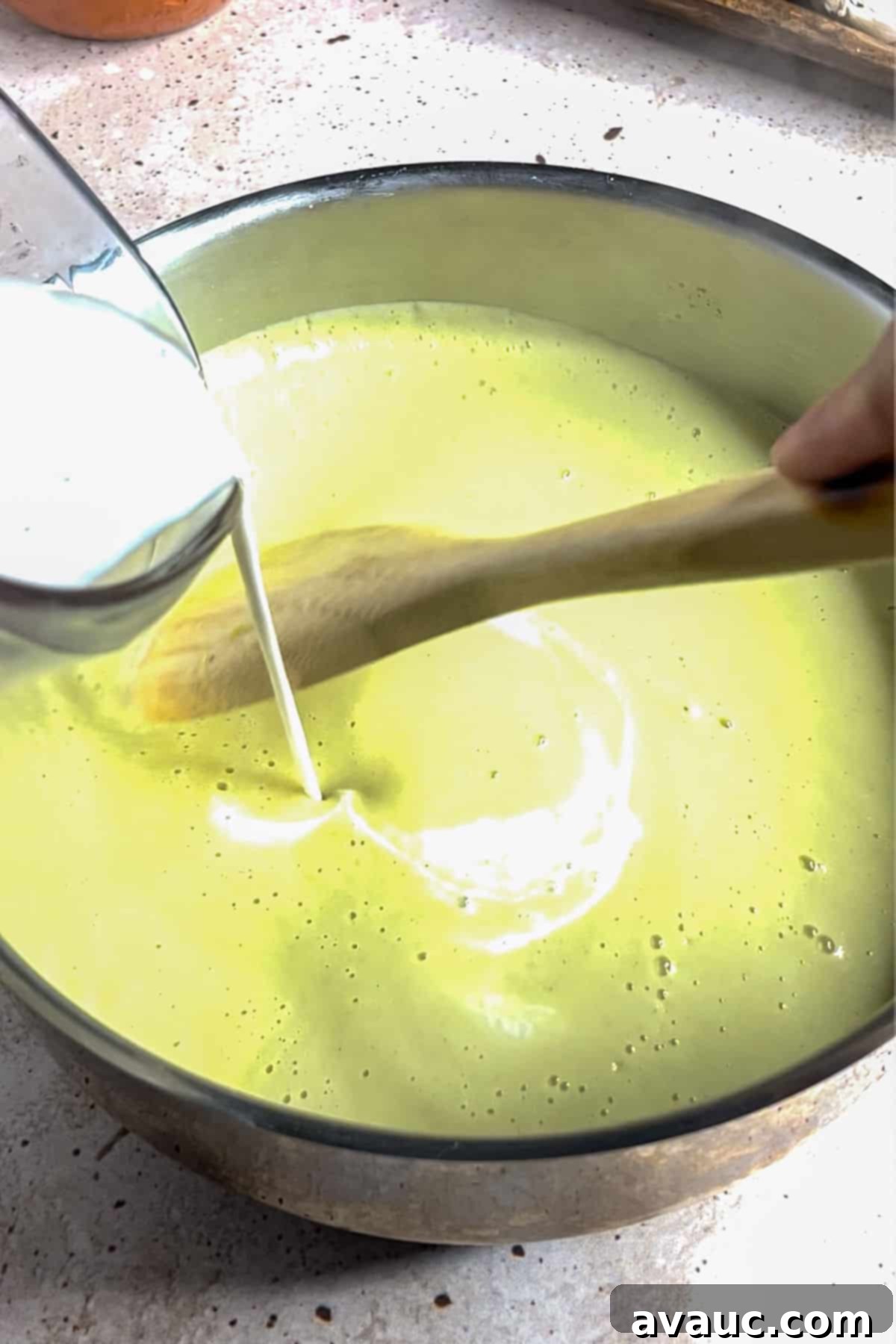 Adding cream to blended creamy onion soup in a pot.